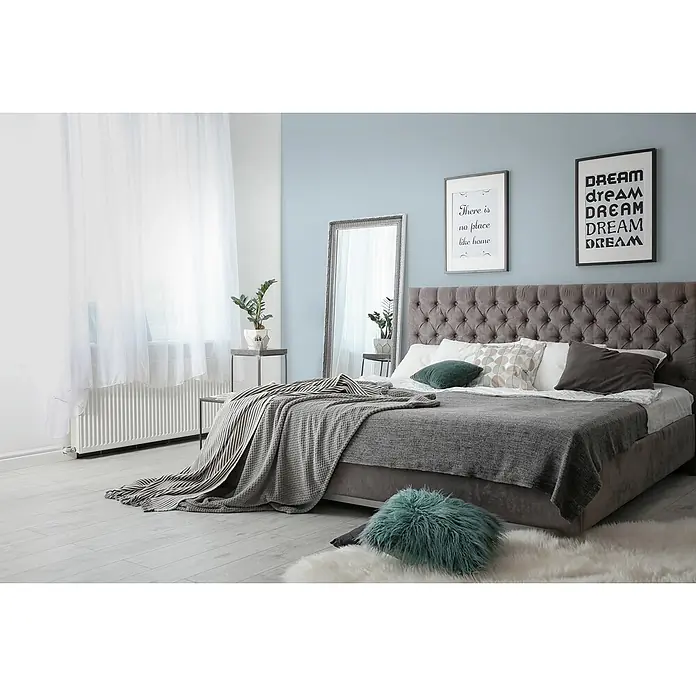 Livingwalls Wandfarbe Blau Ocean Blue DD125884 1l - Blau, Matt, 1 l - Modernes graues Bett mit getuftetem Kopfteil und geschichteter grauer Bettwäsche in einem hellen Schlafzimmer.