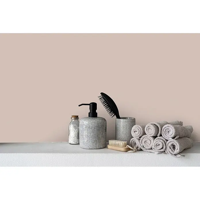 Livingwalls Wandfarbe Beige Chilled Chai Latte 6017 5l - Matt, 5 l - Sortiment aus grau gesprenkeltem Seifenspender und Becher, schwarzer Haarbürste, Holzbürste, Flasche Badesalz und gerollten grauen Handtüchern auf einem Regal.