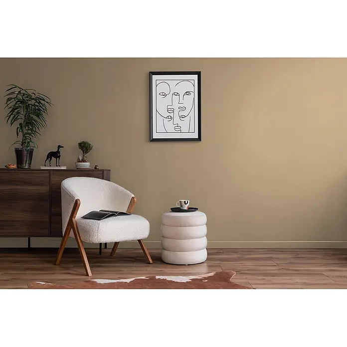 Livingwalls Wandfarbe Beige Sandy Beige DD126081 5l - Beige, Matt, 5 l - Weißer Bouclé-Sessel und gestapelter beiger Ottoman in einem gemütlichen Raum mit Holzmöbeln und abstrakter Kunst.