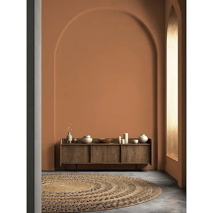 Livingwalls Wandfarbe Orange Dusty Orange DD126152 2,5l - Orange, Matt, 2,5 l - Ein runder, geflochtener Juteteppich mit konzentrischem Muster auf Betonboden in einem Raum mit Terrakottawänden.