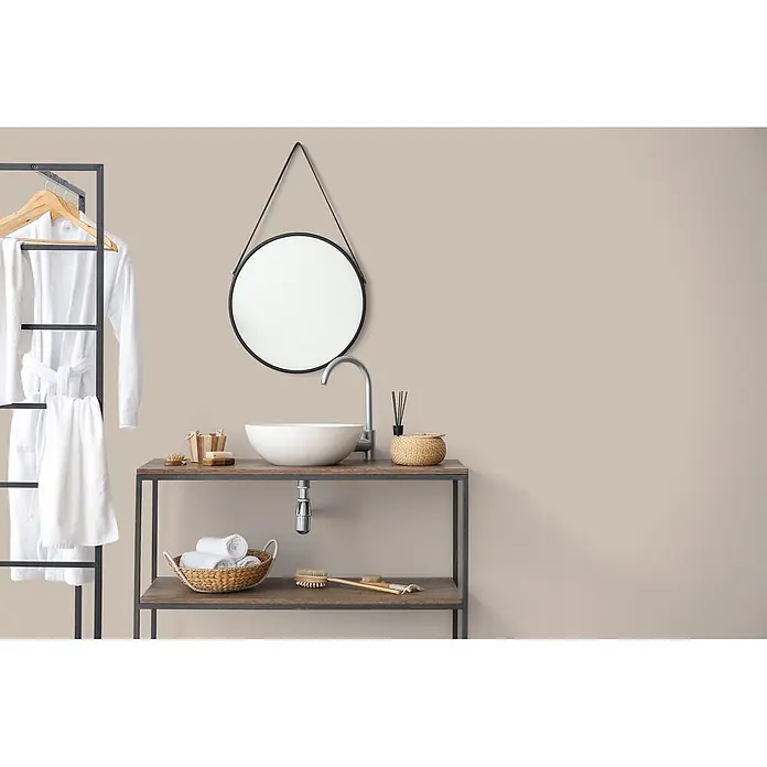 Livingwalls Wandfarbe Beige Seedy Sunflower 6016 2,5l - Matt, 2,5 l - Modernes Bad mit Rundspiegel, weißem Waschbecken auf dunklem Waschtisch mit Ablagen und weißen Bademänteln an schwarzem Ständer.