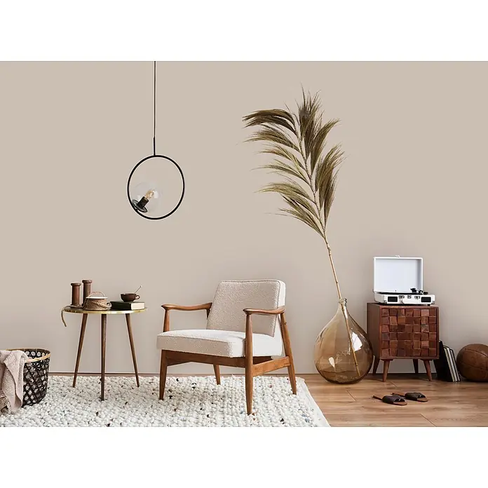 Livingwalls Wandfarbe Beige Seedy Sunflower 6016 2,5l - Matt, 2,5 l - Ein Sessel mit heller Bouclé-Polsterung und Holzrahmen steht auf einem strukturierten Teppich in einem gemütlichen Wohnzimmer.