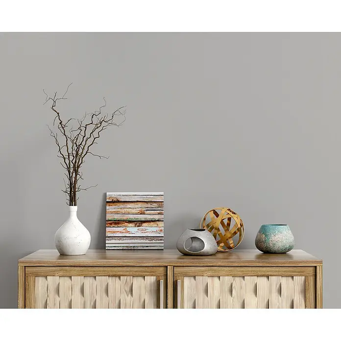 Livingwalls Wandfarbe Grau Shady Spice 1004 2,5l - Matt, 2,5 l - Rustikaler Holzschrank mit dekorativen Lamellentüren, auf dem eine Vase mit Ästen, ein gerahmtes Bild und diverse moderne Deko-Objekte stehen.