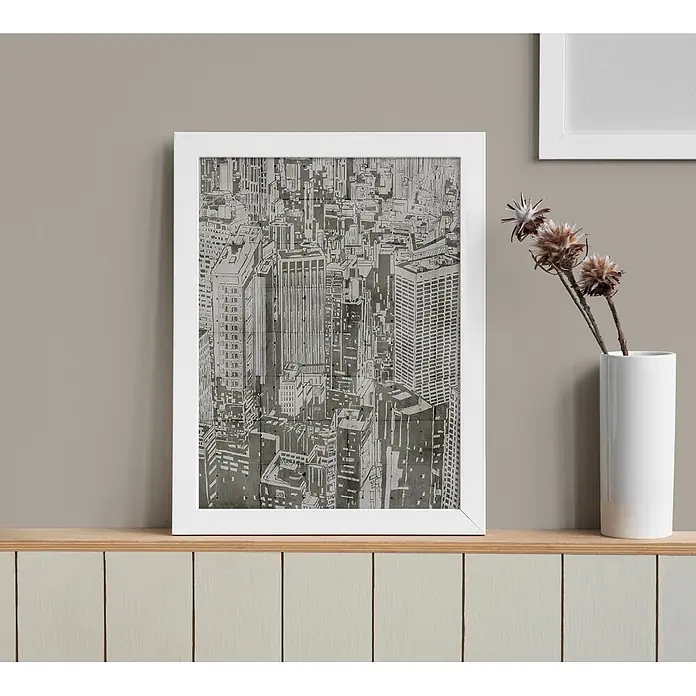 Livingwalls Wandfarbe Taupe Grey Pumpkin 1019 2,5l - Matt, 2,5 l - Weiß gerahmter monochromer Stadtbild-Druck auf einem Holzregal neben einer weißen Vase mit Trockenblumen.
