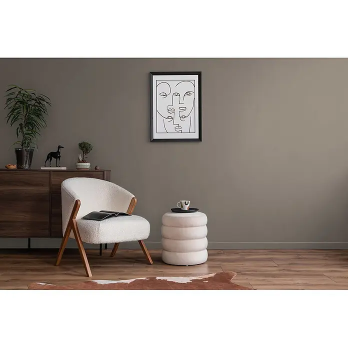 Livingwalls Wandfarbe Braun Calm Taupe DD126007 1l - Braun, Matt, 1 l - Ein stilvoller weißer Bouclé-Sessel und ein gestapelter beiger Hocker bilden eine gemütliche Leseecke in einem modernen Wohnzimmer mit dunklem Holzschrank.