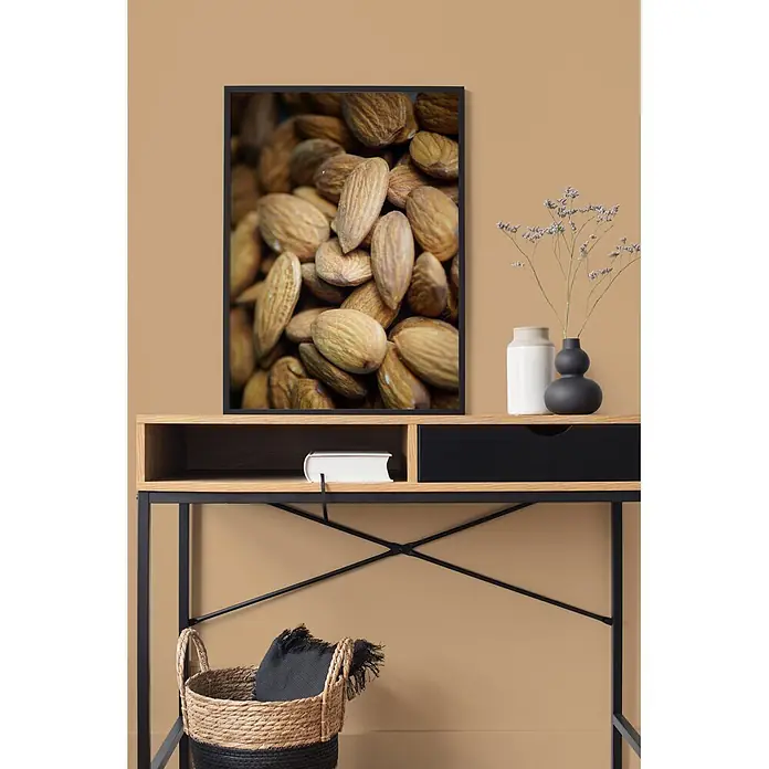 Livingwalls Wandfarbe Braun Active Almond 6004 5l - Matt, 5 l - Schwarzgerahmtes Bild von Mandeln, hängend über einem Holzkonsolentisch.