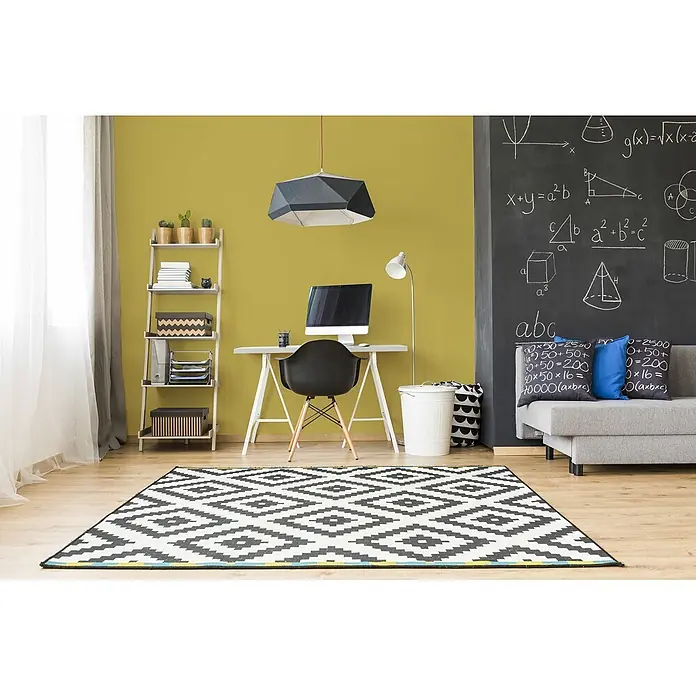 Livingwalls Wandfarbe Grün Gentle Lime DD125984 2,5l - Grün, Matt, 2,5 l - Ein lebhaftes, modernes Heimbüro mit senfgelber Wand, Schreibtisch, Computer, schwarzem Stuhl, Regal und grauem Sofa an einer Tafel.