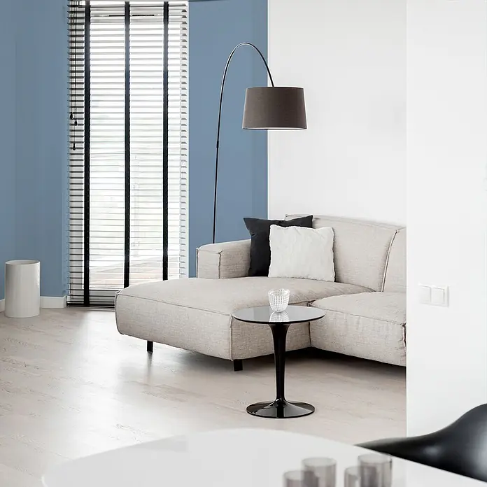 Livingwalls Wandfarbe Blau Ocean Blue DD125891 2,5l - Blau, Matt, 2,5 l - Ein hellbeiges Ecksofa in einem Wohnzimmer, ergänzt durch einen schwarzen Beistelltisch und eine dunkle Stehlampe.