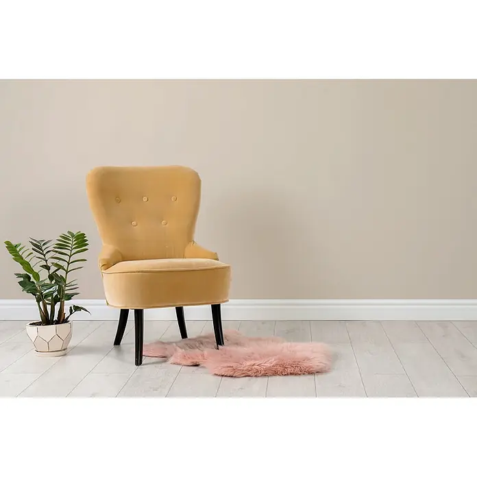 Livingwalls Wandfarbe Beige Sweet Sesame 6000 2,5l - Matt, 2,5 l - Senfgelber Samtsessel mit Knopfheftung und schwarzen Beinen, auf hellem Holzboden mit rosa Kunstfellteppich und Topfpflanze.
