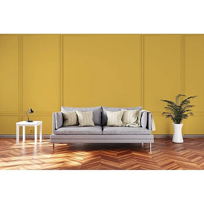 Livingwalls Wandfarbe Gelb Sunny Yellow DD126104 2,5l - Gelb, Matt, 2,5 l - Ein graues Stoffsofa mit gemusterten Kissen, ein weißer Beistelltisch mit schwarzer Lampe und eine grüne Pflanze in einem weißen Topf, alles in einem modernen Wohnzimmer.