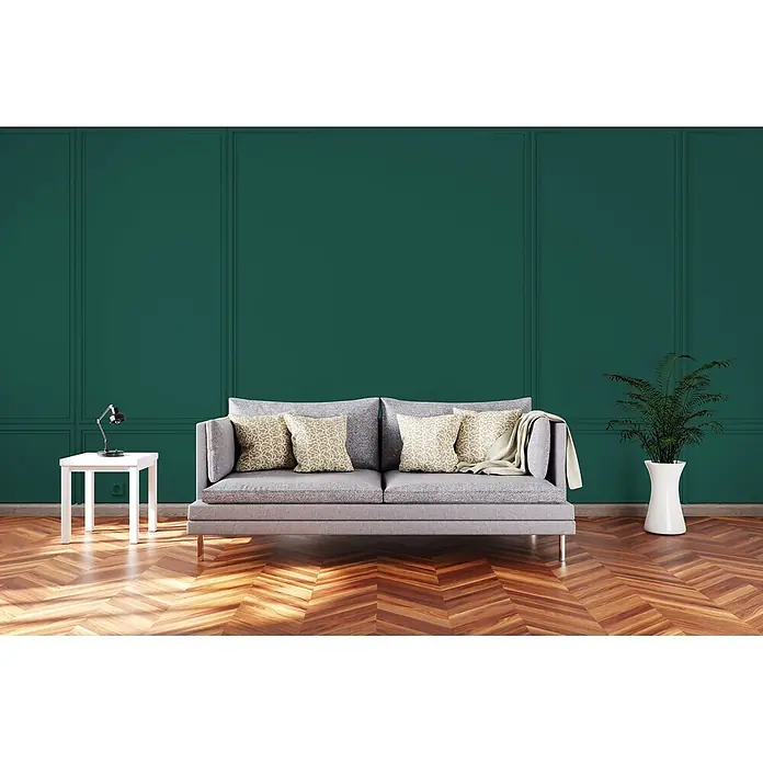 Livingwalls Wandfarbe Grün Emerald Green DD125953 1l - Grün, Matt, 1 l - Graues Sofa mit gemusterten Kissen, Decke, weißem Beistelltisch mit Lampe und Pflanze in einem gemütlichen Raum.