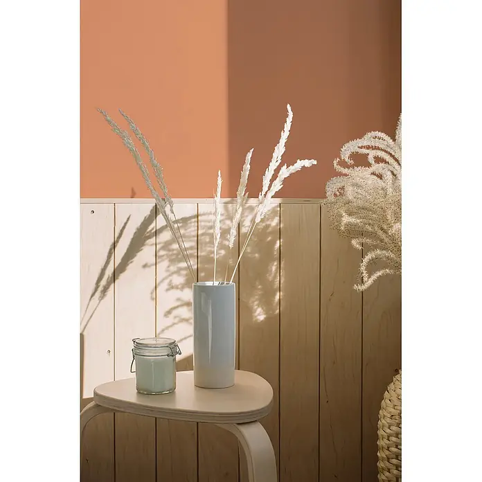 Livingwalls Wandfarbe Orange Dusty Orange DD126145 1l - Orange, Matt, 1 l - Helleblaue Vase mit weißen Trockengräsern und grüner Kerze im Glas auf Holztisch. Sonniger Innenraum.