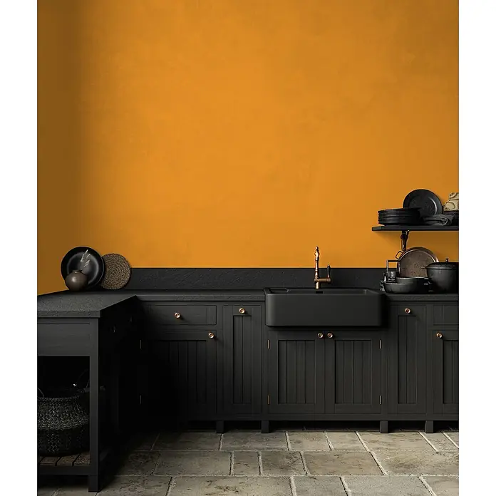 Livingwalls Wandfarbe Gelb Sunny Yellow DD126117 5l - Gelb, Matt, 5 l - Schwarze Küchenschränke, Spüle und Arbeitsplatte mit goldenen Armaturen in einer modernen Küche mit oranger Wand.