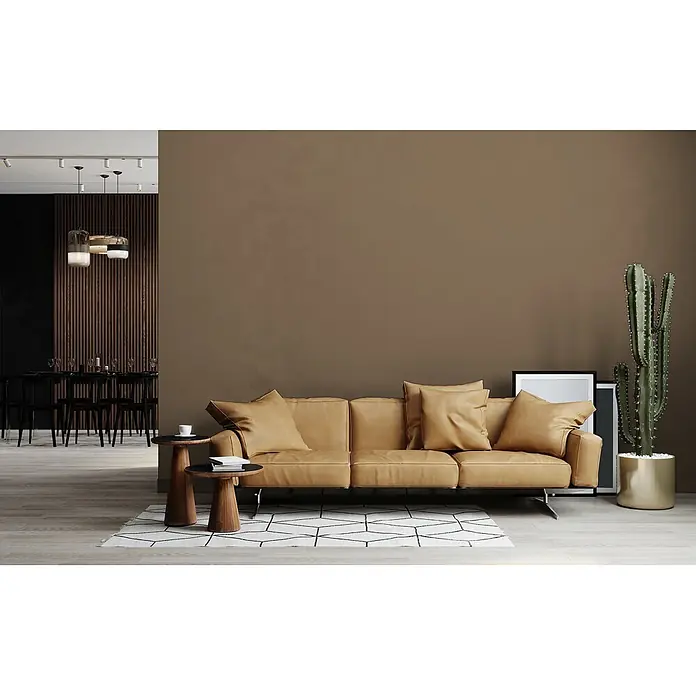 Livingwalls Wandfarbe Braun Mellow Brown DD126037 1l - Braun, Matt, 1 l - Braunes Ledersofa mit Kissen in einem modernen Wohnzimmer auf einem gemusterten Teppich, neben Beistelltischen und einem Kaktus.