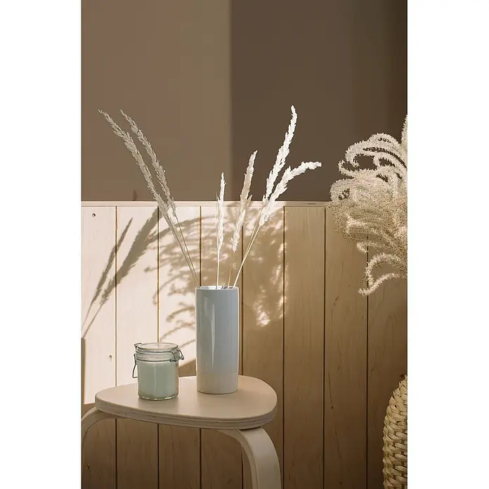 Livingwalls Wandfarbe Braun Mellow Brown DD126037 1l - Braun, Matt, 1 l - Eine hellblau-weiße Keramikvase mit getrocknetem Pampasgras und ein Glas mit Kerze auf einem hellen Holzhocker.