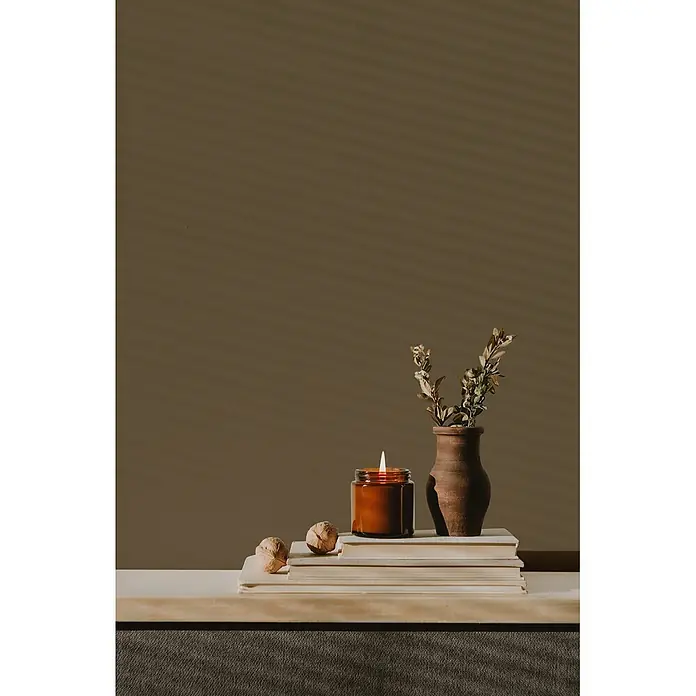 Livingwalls Wandfarbe Braun Mellow Brown DD126040 1l - Braun, Matt, 1 l - Eine brennende Kerze in einem bernsteinfarbenen Glas, eine Terrakotta-Vase mit Trockenpflanzen und ein Bücherstapel als natürliche Heimdekoration.