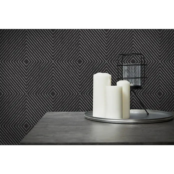 A.S. Création Metropolitan Stories Vliestapete Kachel - Schwarz/Metallic, Grafisch, 10,05 x 0,53 m - Stimmungsvolles Arrangement mit Kerzen und einem dekorativen Kerzenhalter auf einem eleganten Tisch vor einer gemusterten Wand.