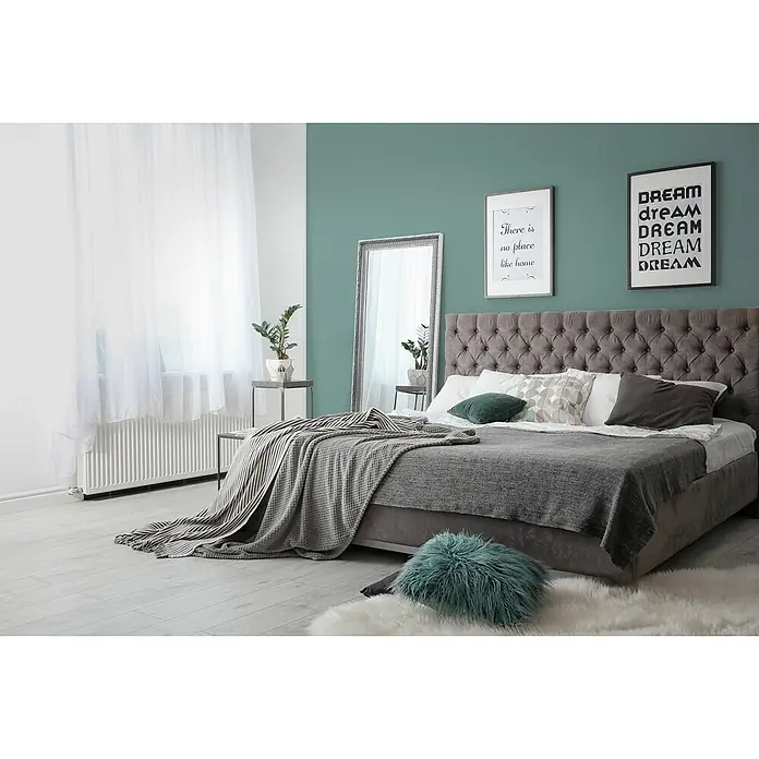 Livingwalls Wandfarbe Grün Soft Green DD125928 5l - Grün, Matt, 5 l - Ein Bett mit grauem, getuftetem Kopfteil, bedeckt mit grauen und gestreiften Decken sowie mehreren gemütlichen Kissen.