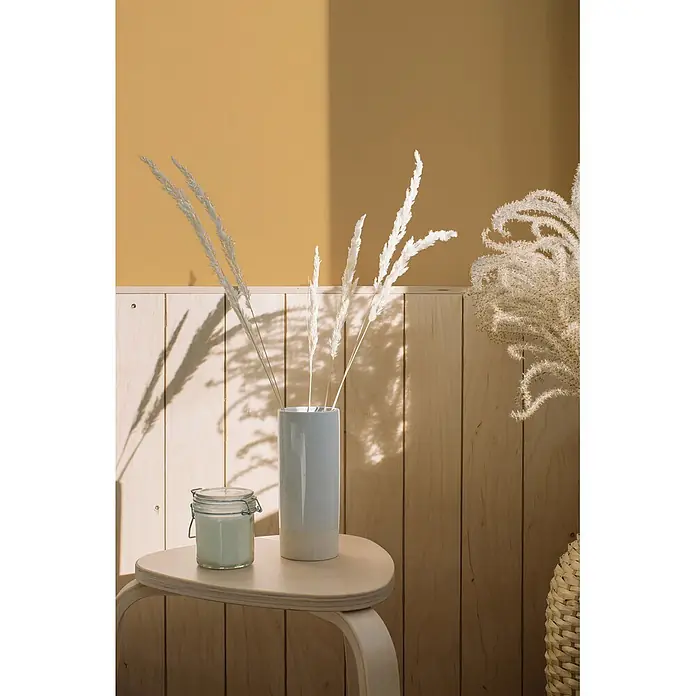 Livingwalls Wandfarbe Gelb Sunny Yellow DD126097 1l - Gelb, Matt, 1 l - Hellblaue und beige Keramikvase mit weißem Trockengras, daneben eine Glaskerze, auf einem Holztisch.