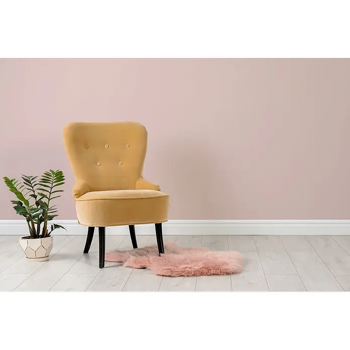 Livingwalls Wandfarbe Beige Sweet Strawberry 7007 2,5l - Beige, Matt, 2,5 l - Ein gelber Samtsessel mit schwarzen Beinen steht auf hellem Holzboden neben einer grünen Pflanze und einem flauschigen rosa Teppich darunter.