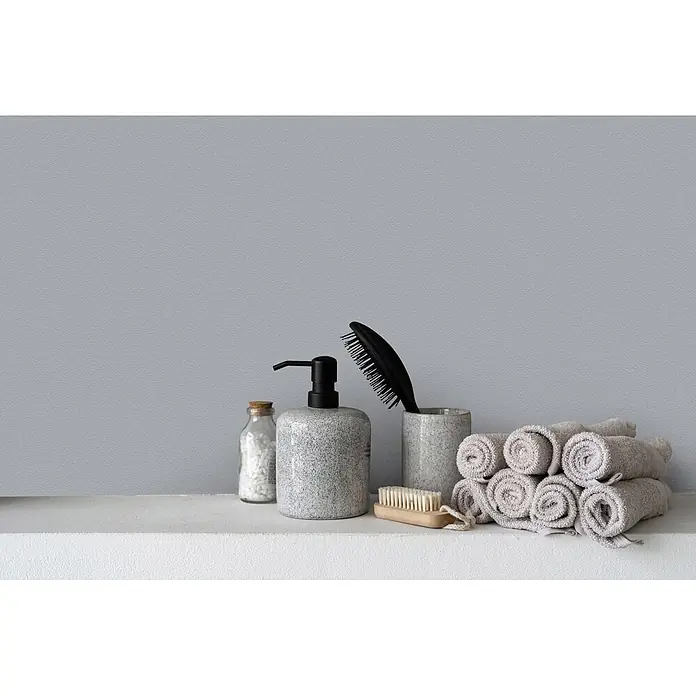 Livingwalls Wandfarbe Grau Sesame Ice Cream 1005 2,5l - Matt, 2,5 l - Badezimmer-Accessoires: grauer gesprenkelter Seifenspender, Tasse mit schwarzer Haarbürste, Holznagelbürste, Badesalze und gerollte beigefarbene Handtücher.