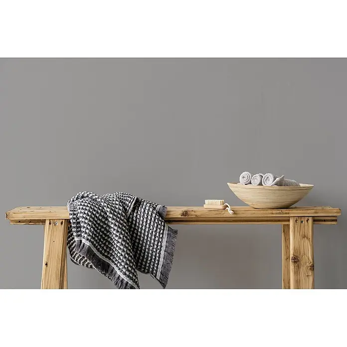 Livingwalls Wandfarbe Grau Attractive Anchovies 1011 2,5l - Matt, 2,5 l - Holzbank mit gemusterter grauer Decke, Holzschale mit gerollten Handtüchern und Naturbürste.