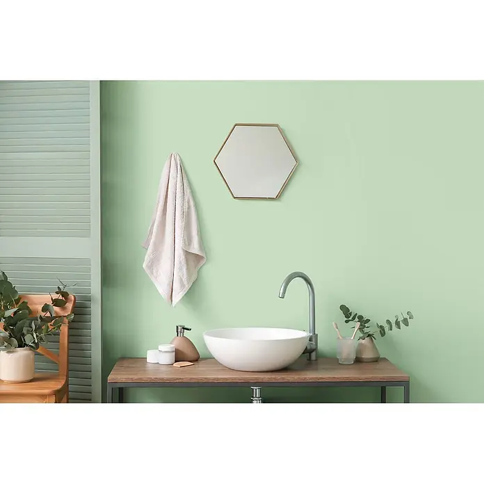 Livingwalls Wandfarbe Grün Woodruff Cream 4007 2,5l - Matt, 2,5 l - Eine moderne Badmöbel-Waschtischanlage mit weißem runden Waschbecken, silberner Armatur und goldenem Sechskantspiegel, ordentlich arrangierten Toilettenartikeln.