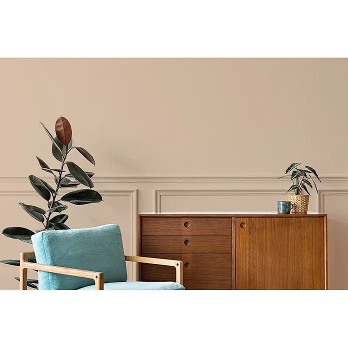 Livingwalls Wandfarbe Beige Nutty Nutmeg 6009 2,5l - Matt, 2,5 l - Türkiser Sessel mit Holzrahmen und dunkles Holzsideboard mit Schubladen, mit Pflanzen dekoriert.