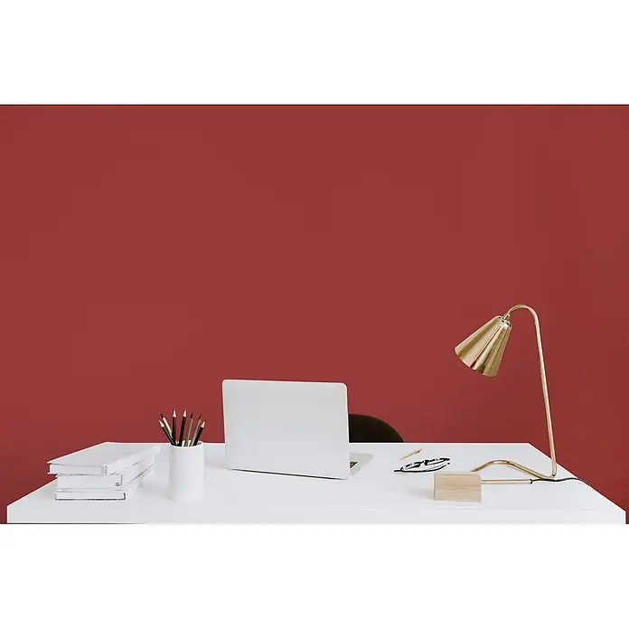 Livingwalls Wandfarbe Rot Cheeky Chilli 7005 2,5l - Rot, Matt, 2,5 l - Ein moderner weißer Schreibtisch mit Laptop, Büchern, Stiften und einer goldenen Lampe vor einer roten Wand.