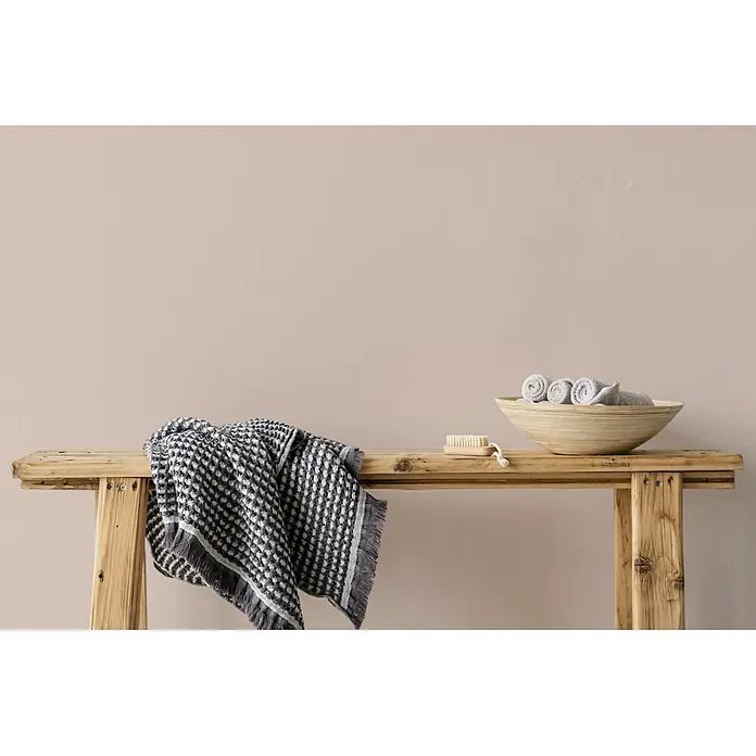Livingwalls Wandfarbe Beige Himalaya Salt 7000 5l - Matt, 5 l - Dunkelgrau-weißes Waffeltuch auf einer Holzbank, neben einer Schale mit Handtüchern und einer Bürste.