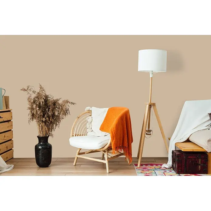 Livingwalls Wandfarbe Beige Flat White Coffee 6002 5l - Matt, 5 l - Ein gemütlicher Raum mit natürlichem Rattansessel, weißem Kissen und oranger Decke, neben einer hölzernen Stehlampe.