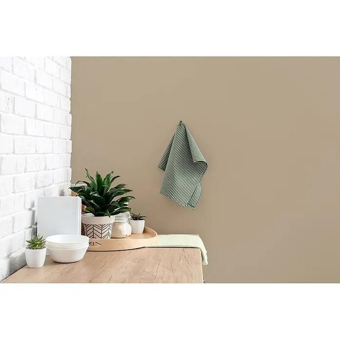 Livingwalls Wandfarbe Beige Flat White Coffee 6002 5l - Matt, 5 l - Ein grün-weiß gestreiftes Geschirrtuch hängt an einer beigen Wand über einer Holztheke mit Pflanzen und Schüsseln.