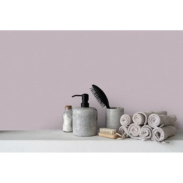 Livingwalls Wandfarbe Violett Leafy Lavender 2004 5l - Matt, 5 l - Grau gesprenkelte Badaccessoires, Holzbürste und gerollte Handtücher auf einem weißen Regal vor rosa Wand.