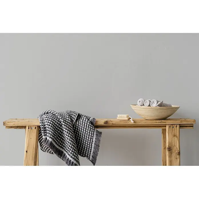 Livingwalls Wandfarbe Grau Pure Pitaya 1003 2,5l - Matt, 2,5 l - Holzhocker mit grau gemustertem Handtuch, Holzbürste und Holzschale mit gerollten Handtüchern.
