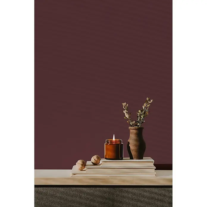 Livingwalls Wandfarbe Rot Lovely Rose DD125814 5l - Rot, Matt, 5 l - Brennende Kerze in einem bernsteinfarbenen Glasgefäß, auf einem Bücherstapel, neben einer Tonvase und Walnüssen.