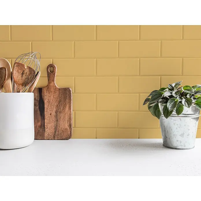 Livingwalls Wandfarbe Gelb Playful Pineapple 5005 5l - Matt, 5 l - Küchenarbeitsplatte mit weißem Utensilienhalter, Holzschneidebrett und einer Pflanze im Metalltopf vor gelben Metrofliesen.