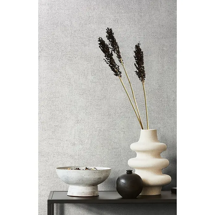 Livingwalls Vliestapete Uni, hellgrau -  - Strukturierte beigefarbene Vase mit getrockneten dunklen Zweigen, auf einem Regal neben weißer Schale und schwarzer Vase.
