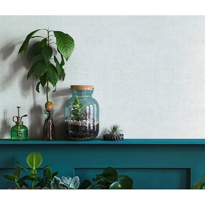 Livingwalls Vliestapete Uni, weiß -  - Blaues Glas-Terrarium mit Korkdeckel, das kleine Pflanzen und Kieselsteine enthält, auf einem teal-farbenen Regal.