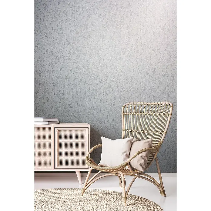 Livingwalls Vliestapete Grafisch, weiß - 10.050 x 530 mm - Eine gemütliche Zimmerecke mit hellblauer Blumentapete, einem rosa Schrank mit Rattan-Details und einem Rattansessel mit beigen Kissen auf einem Webteppich.