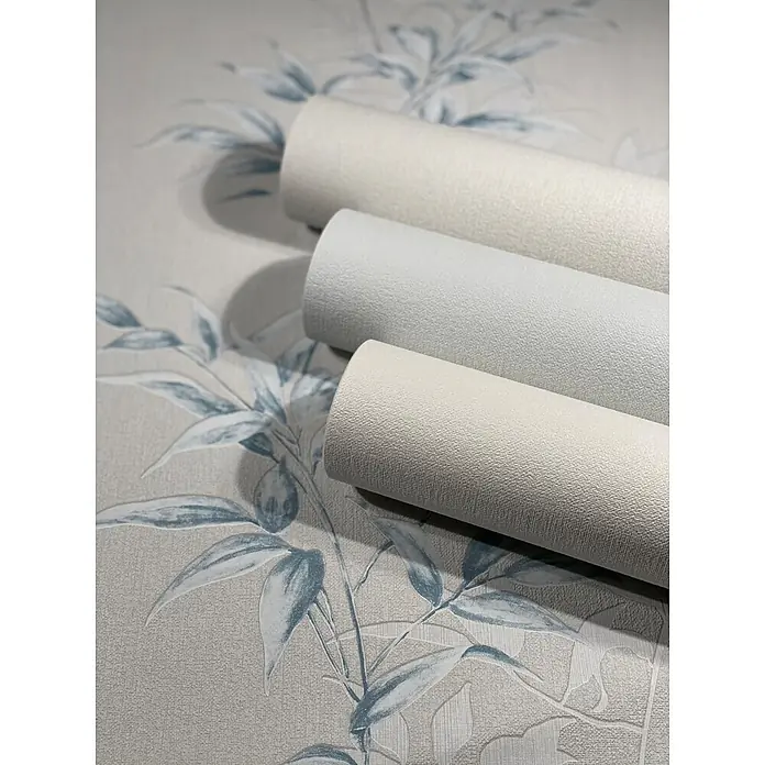 Livingwalls Vliestapete Floral, greige, blau - blau, 10.050 x 530 mm - Drei Rollen strukturierter, heller Tapete liegen auf einer gemusterten Tapete mit blauen Blattmotiven.