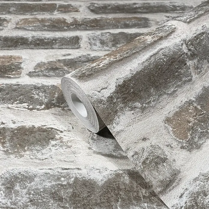 Livingwalls Vliestapete Steinoptik, beige-braun - 10.050 x 530 mm - Strukturierte Tapetenrolle mit Ziegelsteinmuster in Grau- und Brauntönen, teilweise abgerollt.