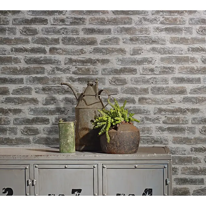 Livingwalls Vliestapete Steinoptik, beige-braun - 10.050 x 530 mm - Industrieller grauer Metallschrank mit Staufächern, dunklen Nummern und Vintage-Objekten darauf, vor einer Ziegelwand.