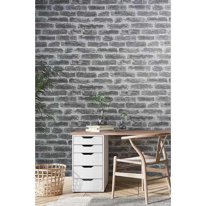 Livingwalls Vliestapete Steinoptik, greige - 10.050 x 530 mm - Graue Ziegelwand mit unregelmäßiger Textur, mit modernem Home-Office-Schreibtisch und Stuhl.