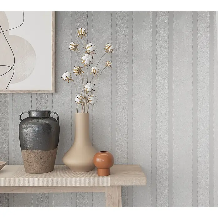 Livingwalls Vliestapete Streifen, weiß metallic - 10.050 x 530 mm - Ein heller Holzkonsolentisch mit dekorativen Vasen und gerahmter Kunst vor einer gestreiften Wand.