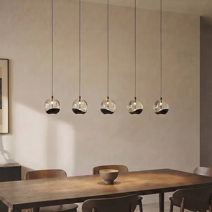 Lucande Pendelleuchte Hayley - klar / transparent, klar, Schwarz - Fünf moderne Pendelleuchten mit klaren Glaskugeln und schwarzen welligen Sockeln hängen elegant über einem Holztisch.