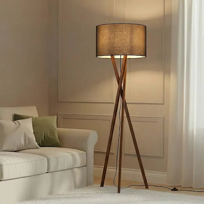 Lucande Stehleuchte Auriane - Holz dunkel, schwarz, E27 - Große Stehlampe mit schwarzem Stoff-Trommelschirm und Naturholz-Dreibeingestell, beleuchtet ein Wohnzimmer neben einem cremefarbenen Sofa.