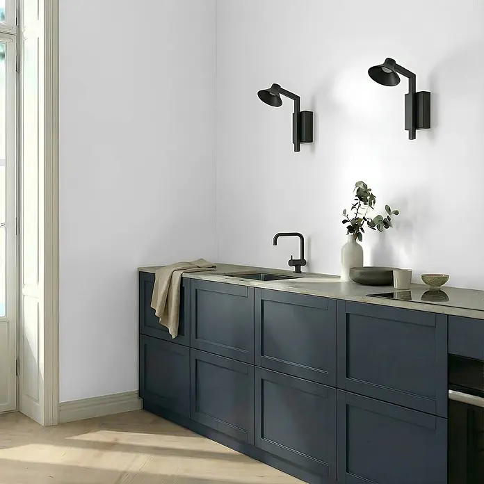 Lucande Wandleuchte Steve - schwarz, schwarz - Eine moderne Küche mit dunkelblauen Unterschränken, heller Arbeitsplatte, schwarzem Wasserhahn und zwei schwarzen Wandleuchten. Spüle und Kochfeld sind integriert.