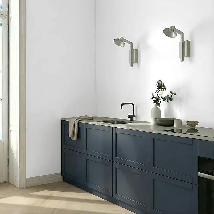Lucande Wandleuchte Steve - alu / grau / zink, alu / grau / zink - Dunkelblaue Küchenschränke mit heller Arbeitsplatte, integrierter Spüle, schwarzem Wasserhahn und Kochfeld in einer modernen Küchenecke.