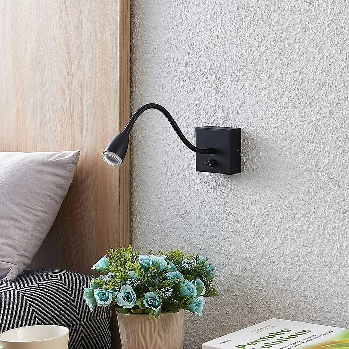 Lindby Wandleuchte Jolka - L x B x H: 30 x 7 x 15 cm, schwarz, schwarz - Schwarze Wandleselampe aus Metall mit flexiblem Schwanenhals und Kippschalter, neben einem Holzkopfteil platziert.