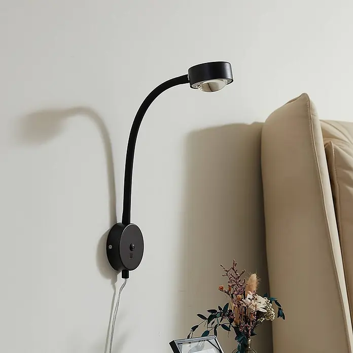 Lindby Wandleuchte Jyla - L x B x H: 26,5 x 8 x 25 cm, schwarz, schwarz, 2GX53 - Schwarze wandmontierte Leselampe mit flexiblem Schwanenhals, über einem Nachttisch neben einem cremefarbenen Kopfteil.